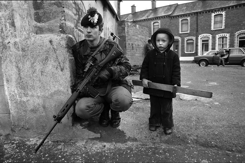 A young boy stands beside a British soldier on patrol (Image: Getty)